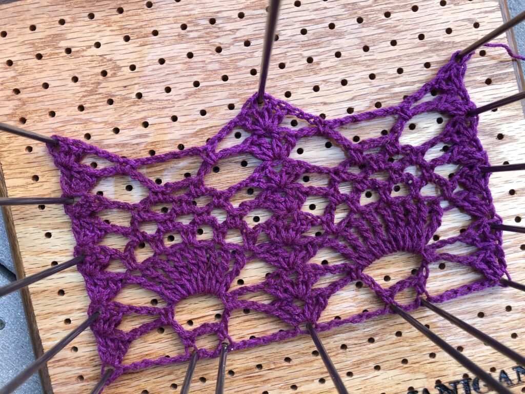 Purple thread worked into a pineapple lace motif pinned onto a board.