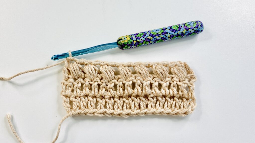 Small swatch of puff stitch with cream yarn and blue crochet hook